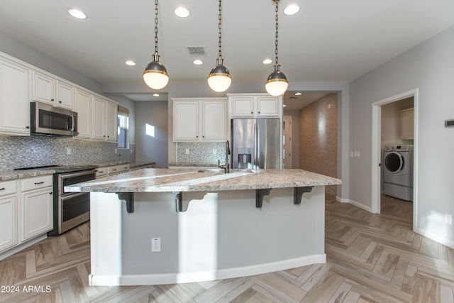 kitchen with washer / dryer, stainless steel appliances, white cabinetry, and a center island with sink