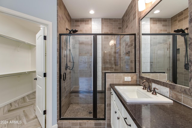 bathroom with vanity, tile walls, a shower with shower door, and backsplash