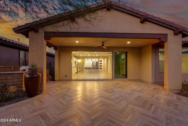 back house at dusk with ceiling fan and a patio