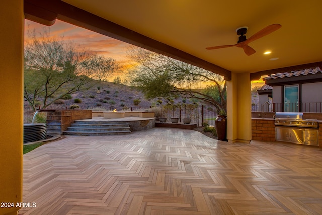 patio terrace at dusk with ceiling fan, a grill, and exterior kitchen