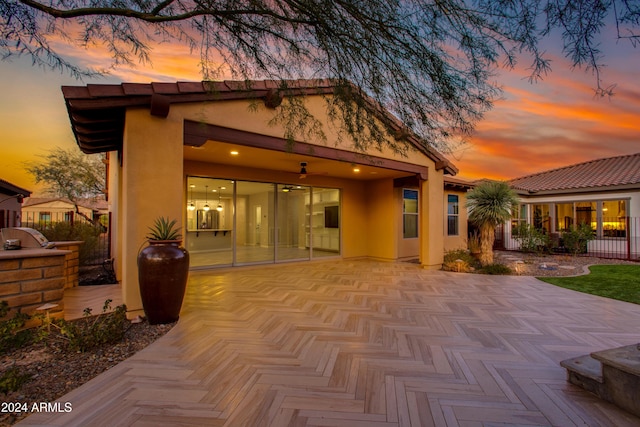 back house at dusk featuring ceiling fan and a patio area