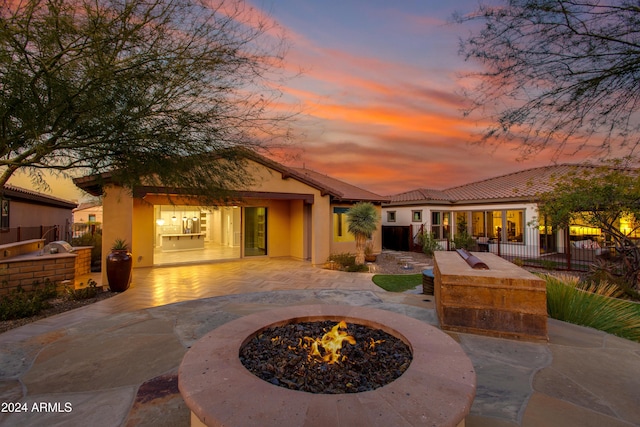 back house at dusk with a patio area, exterior kitchen, and an outdoor fire pit