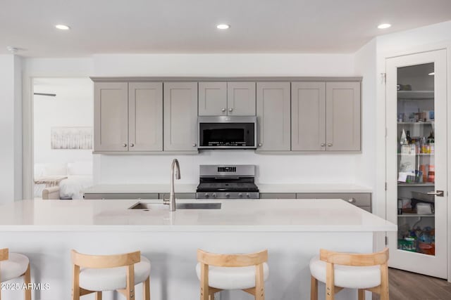 kitchen with a breakfast bar, a sink, light countertops, gray cabinets, and stainless steel appliances