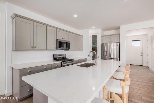 kitchen featuring a sink, gray cabinets, appliances with stainless steel finishes, and a breakfast bar