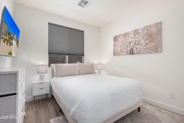 bedroom with baseboards, visible vents, and wood finished floors