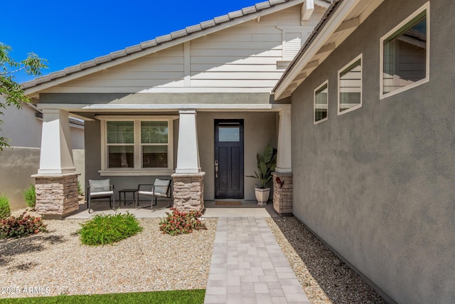 property entrance featuring covered porch, a tiled roof, and stucco siding