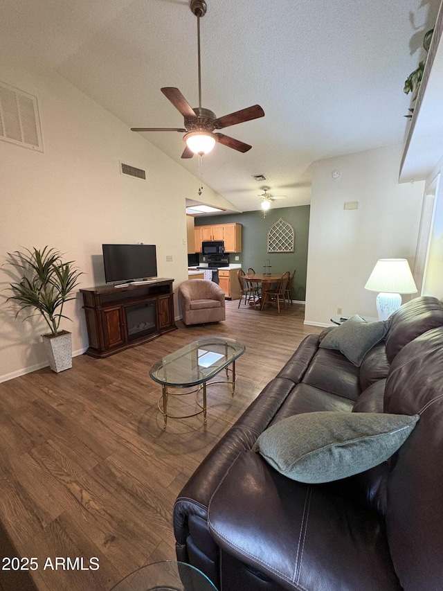 living room with wood-type flooring, vaulted ceiling, ceiling fan, and a textured ceiling