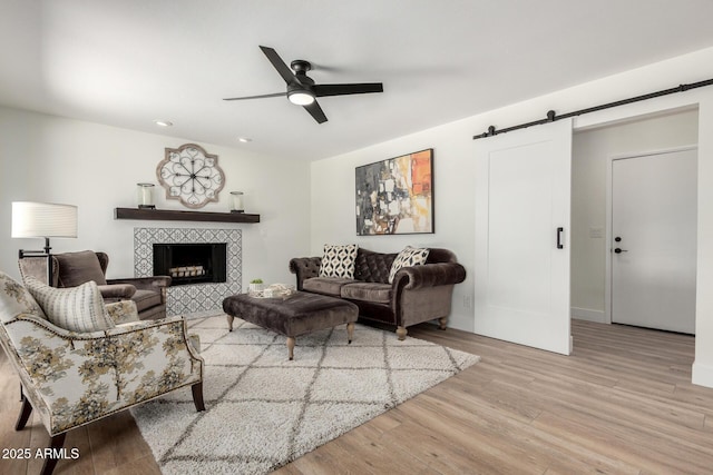 5211 E Winchcomb Dr, Scottsdale, AZ 85254 - living area featuring a barn door, ceiling fan, wood finished floors, a tiled fireplace, and recessed lighting