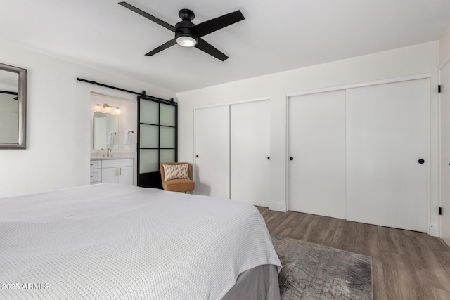 5211 E Winchcomb Dr, Scottsdale, AZ 85254 - bedroom featuring multiple closets, a barn door, wood finished floors, connected bathroom, and ceiling fan
