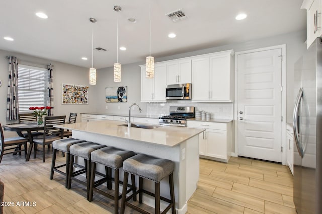 kitchen with white cabinetry, a center island with sink, stainless steel appliances, sink, and pendant lighting