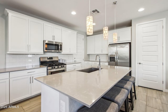 kitchen featuring a center island with sink, sink, stainless steel appliances, and pendant lighting