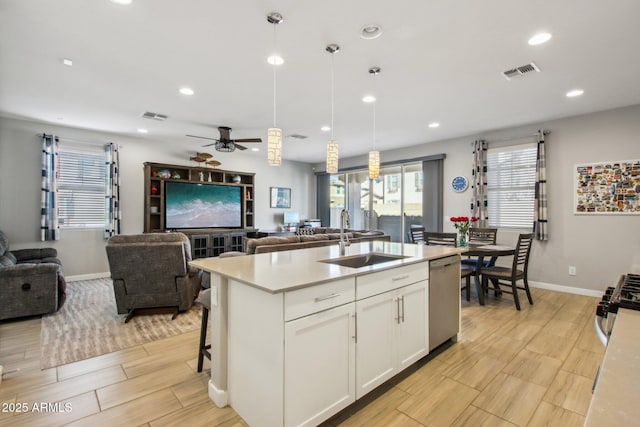 kitchen with appliances with stainless steel finishes, an island with sink, white cabinets, decorative light fixtures, and sink