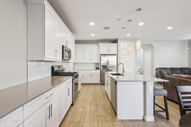 kitchen with a center island with sink, stainless steel appliances, pendant lighting, sink, and white cabinetry
