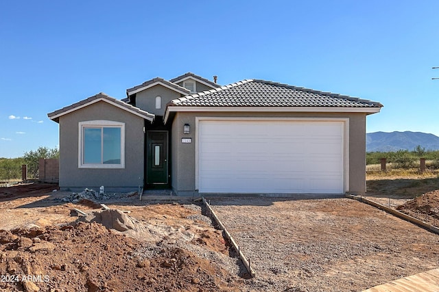 single story home with a garage, driveway, a tile roof, a mountain view, and stucco siding