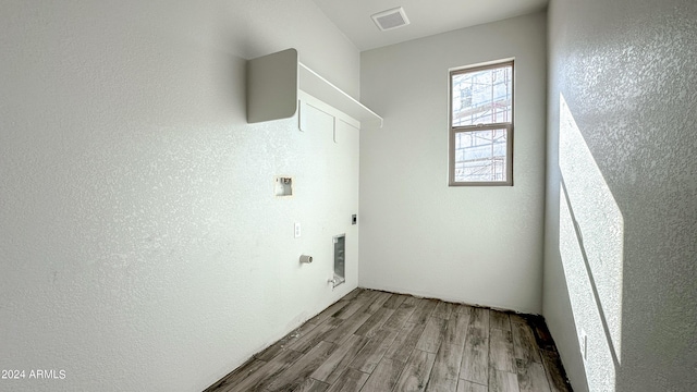 laundry area featuring laundry area, visible vents, a textured wall, wood finished floors, and electric dryer hookup