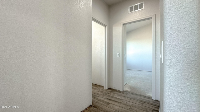 hall with visible vents, a textured wall, and light wood finished floors