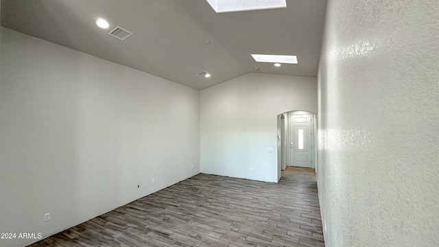 empty room with vaulted ceiling with skylight, light wood-style flooring, visible vents, and arched walkways