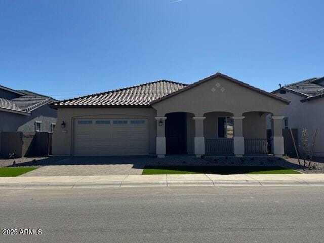 mediterranean / spanish-style home featuring a porch, an attached garage, driveway, a tiled roof, and stucco siding