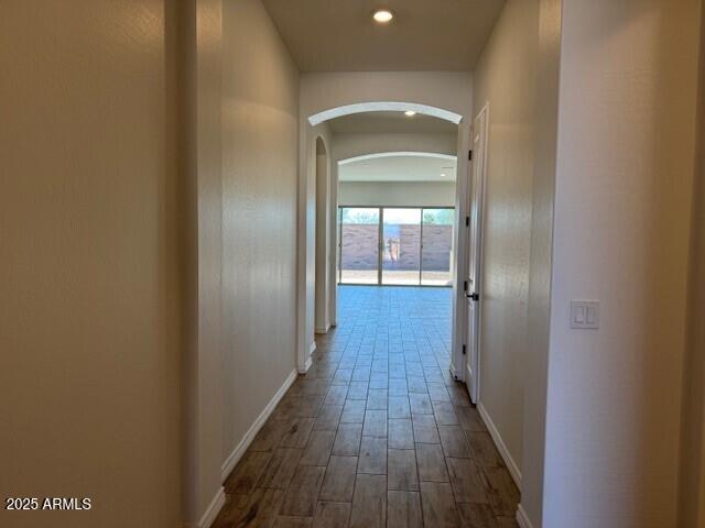corridor with arched walkways, recessed lighting, wood finished floors, and baseboards