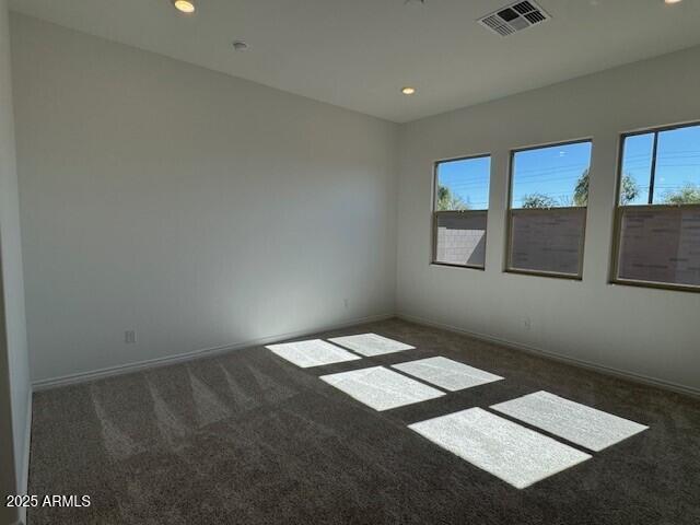 unfurnished room with dark colored carpet, a healthy amount of sunlight, and visible vents