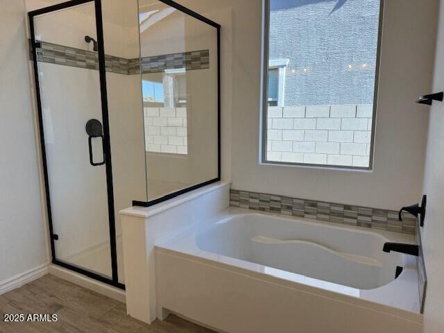 full bath featuring wood finished floors, a shower stall, and a bath