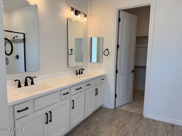 full bath featuring double vanity, a spacious closet, a sink, and wood finished floors