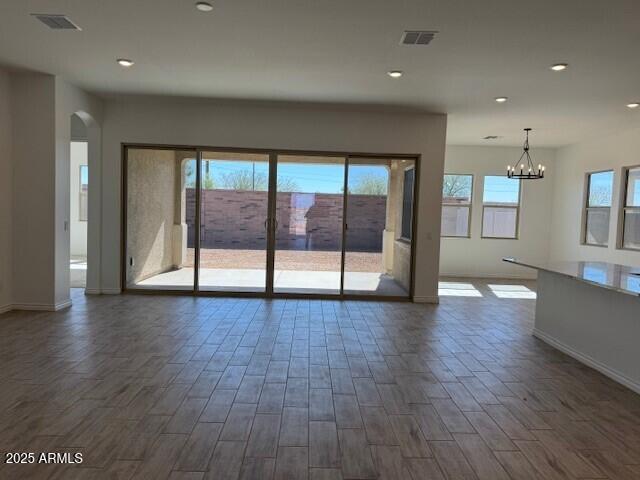 spare room featuring dark wood-style floors, arched walkways, visible vents, and plenty of natural light