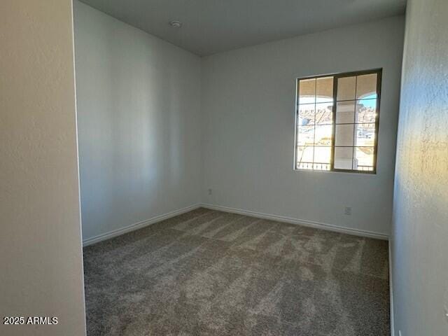 unfurnished room with baseboards and dark carpet