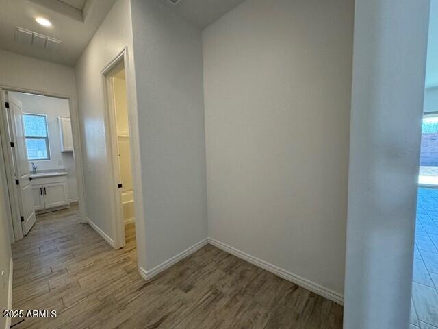 hall featuring light wood-style floors, attic access, visible vents, and baseboards