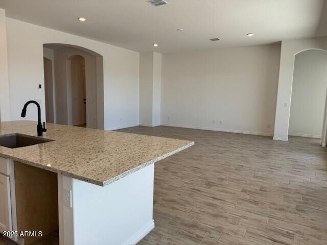 kitchen with arched walkways, a sink, open floor plan, light stone countertops, and an island with sink