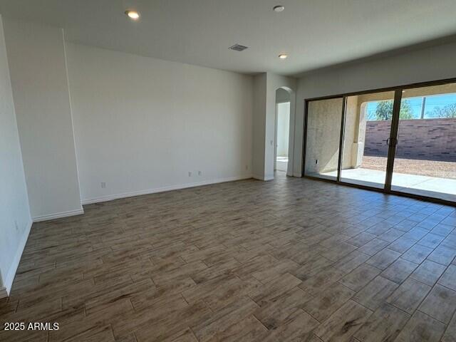 unfurnished room featuring arched walkways, dark wood-style flooring, visible vents, and baseboards