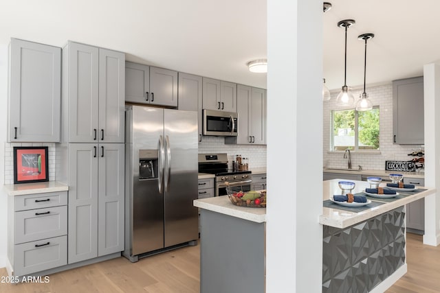 kitchen featuring appliances with stainless steel finishes, gray cabinetry, tasteful backsplash, a sink, and light wood-style flooring