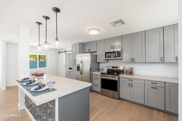 kitchen with stainless steel appliances, gray cabinetry, backsplash, light wood-style floors, and a barn door