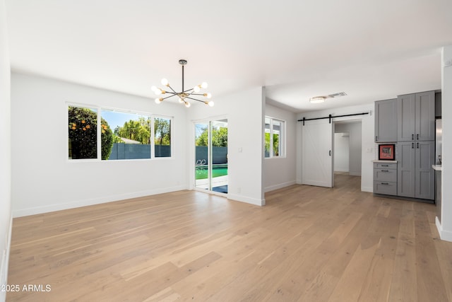 unfurnished living room with a barn door, a chandelier, light wood finished floors, and baseboards