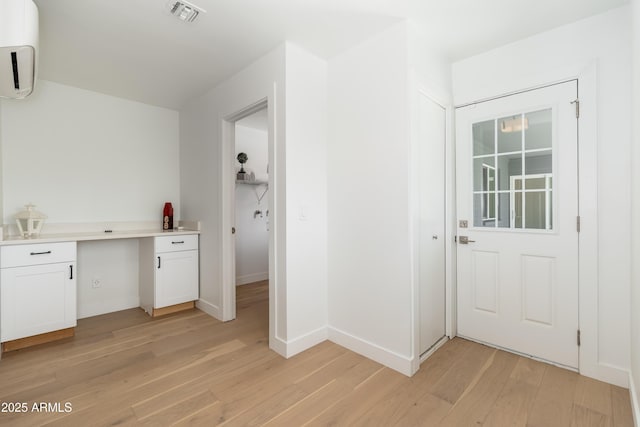 clothes washing area featuring light wood-type flooring, a wall unit AC, and baseboards