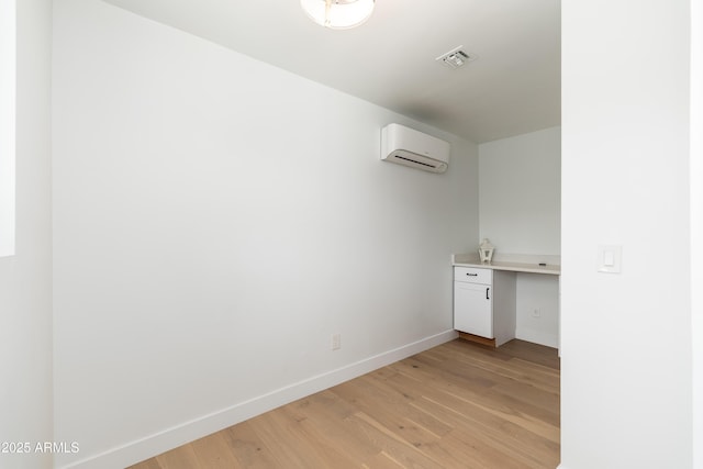 laundry area featuring light wood-type flooring, an AC wall unit, and baseboards