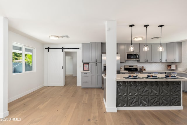 kitchen with gray cabinets, stainless steel appliances, a barn door, decorative backsplash, and light wood-type flooring