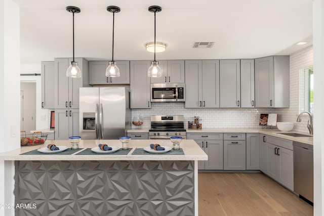 kitchen with appliances with stainless steel finishes, a sink, gray cabinets, and light wood finished floors