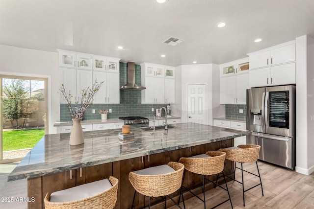 kitchen featuring wall chimney exhaust hood, a large island, appliances with stainless steel finishes, a sink, and backsplash