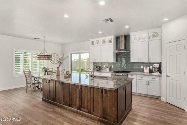 kitchen featuring a sink, light wood-style floors, backsplash, wall chimney exhaust hood, and gas range