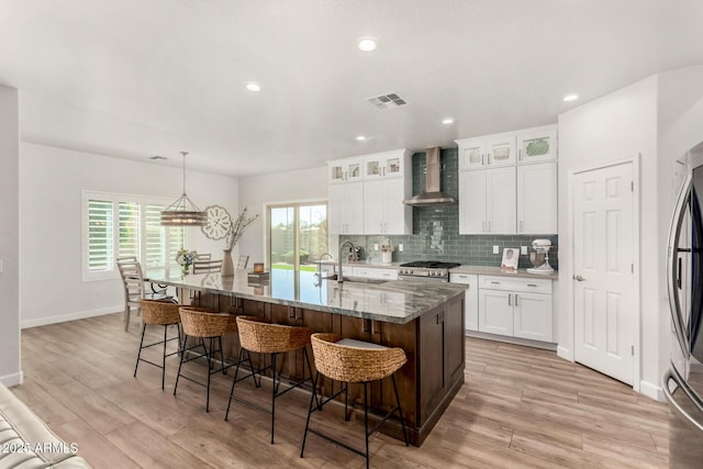 kitchen with stainless steel range with gas cooktop, light wood-style flooring, backsplash, a sink, and wall chimney exhaust hood