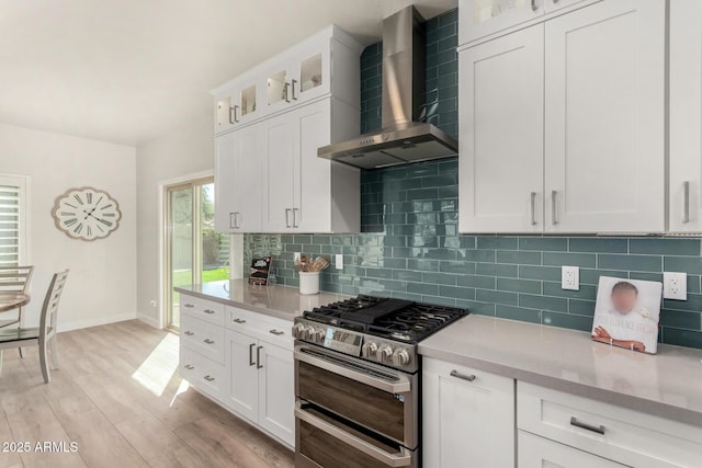 kitchen with wall chimney exhaust hood, double oven range, light countertops, and backsplash