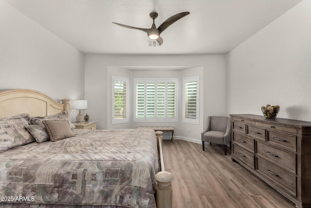 bedroom with a ceiling fan, visible vents, baseboards, and wood finished floors