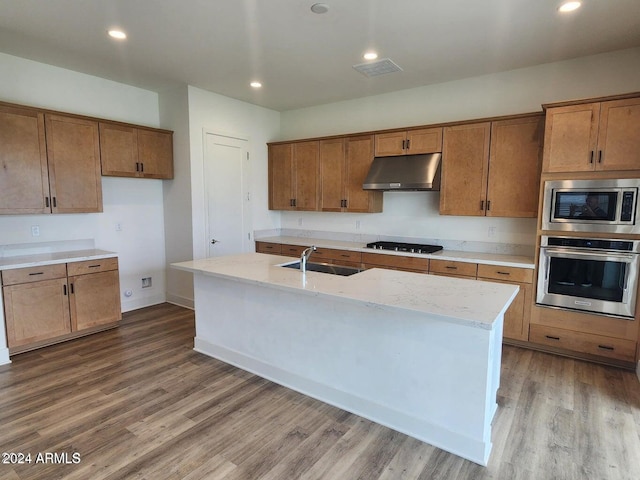 kitchen featuring appliances with stainless steel finishes, hardwood / wood-style floors, sink, a kitchen island with sink, and light stone countertops