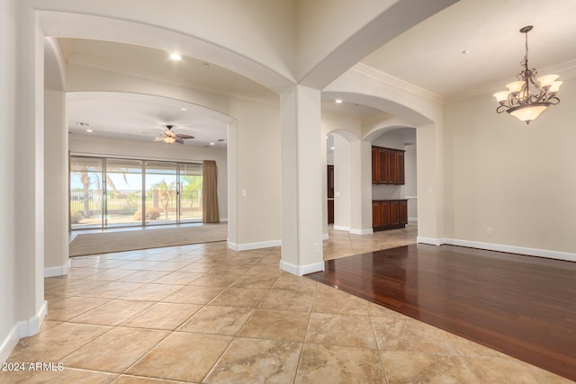 empty room featuring ornamental molding, light wood-type flooring, and ceiling fan with notable chandelier