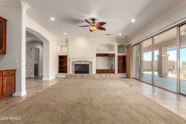 unfurnished living room with a tile fireplace, ornamental molding, ceiling fan, light tile patterned flooring, and built in features