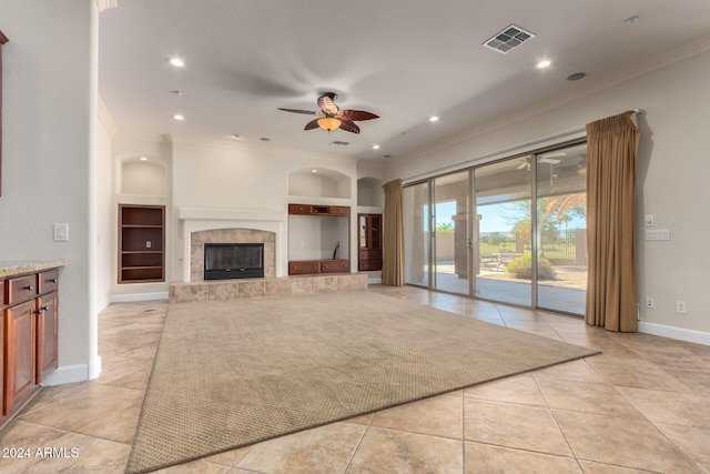 unfurnished living room with built in shelves, a premium fireplace, light tile patterned floors, ornamental molding, and ceiling fan