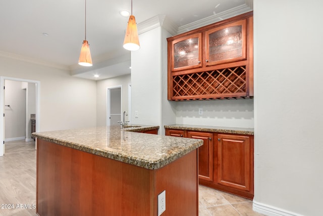 kitchen with sink, ornamental molding, light stone countertops, hanging light fixtures, and a kitchen island with sink