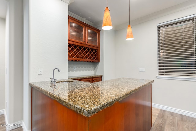 bar with dark stone counters, sink, ornamental molding, pendant lighting, and light hardwood / wood-style flooring