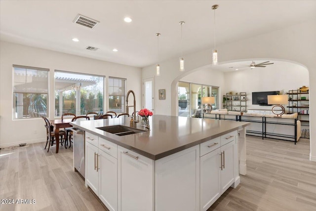 kitchen with sink, a kitchen island with sink, white cabinetry, light hardwood / wood-style flooring, and decorative light fixtures